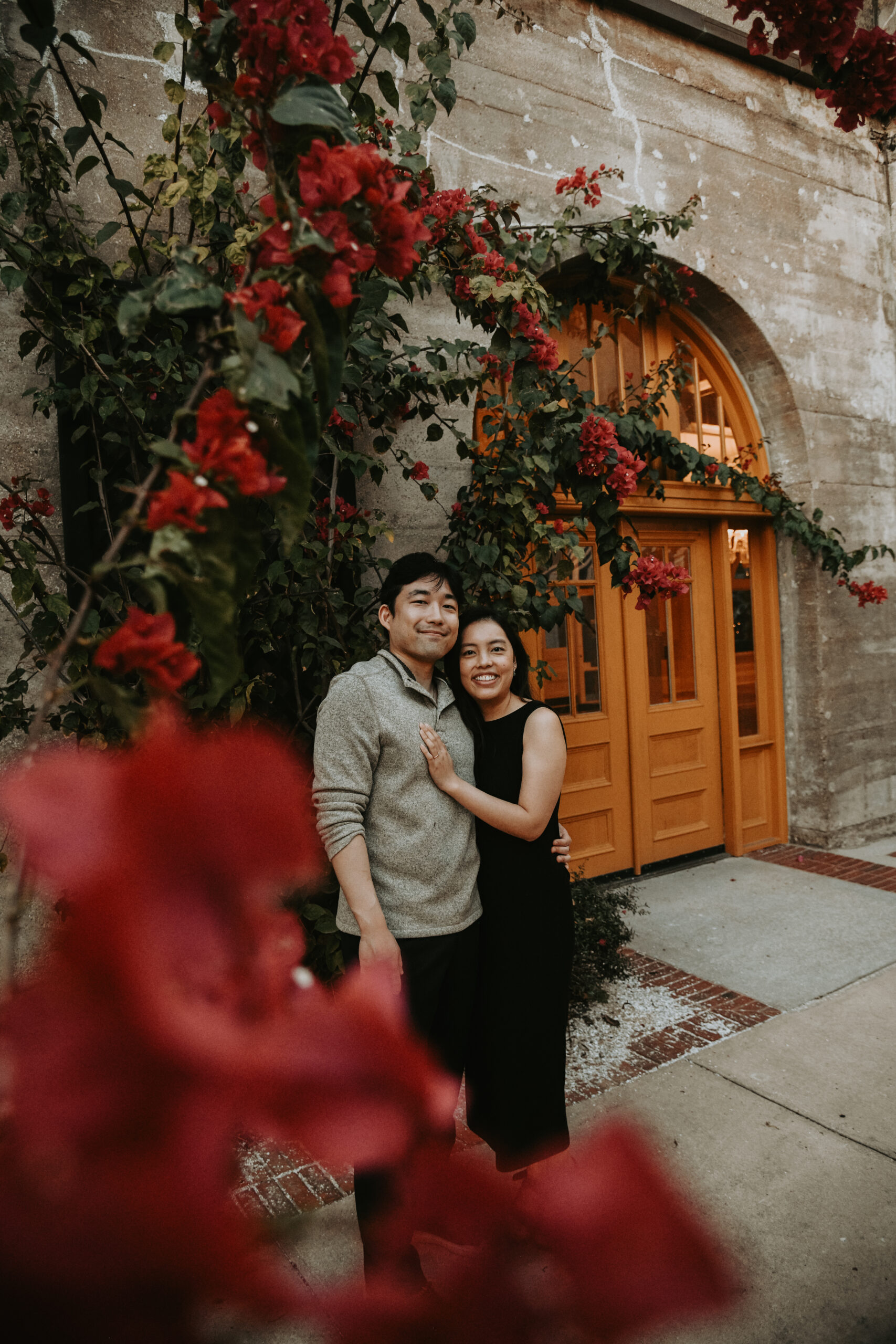 An engaged couple embracing beneath red bougainvillea framing a yellow arched doorway in historic St. Augustine