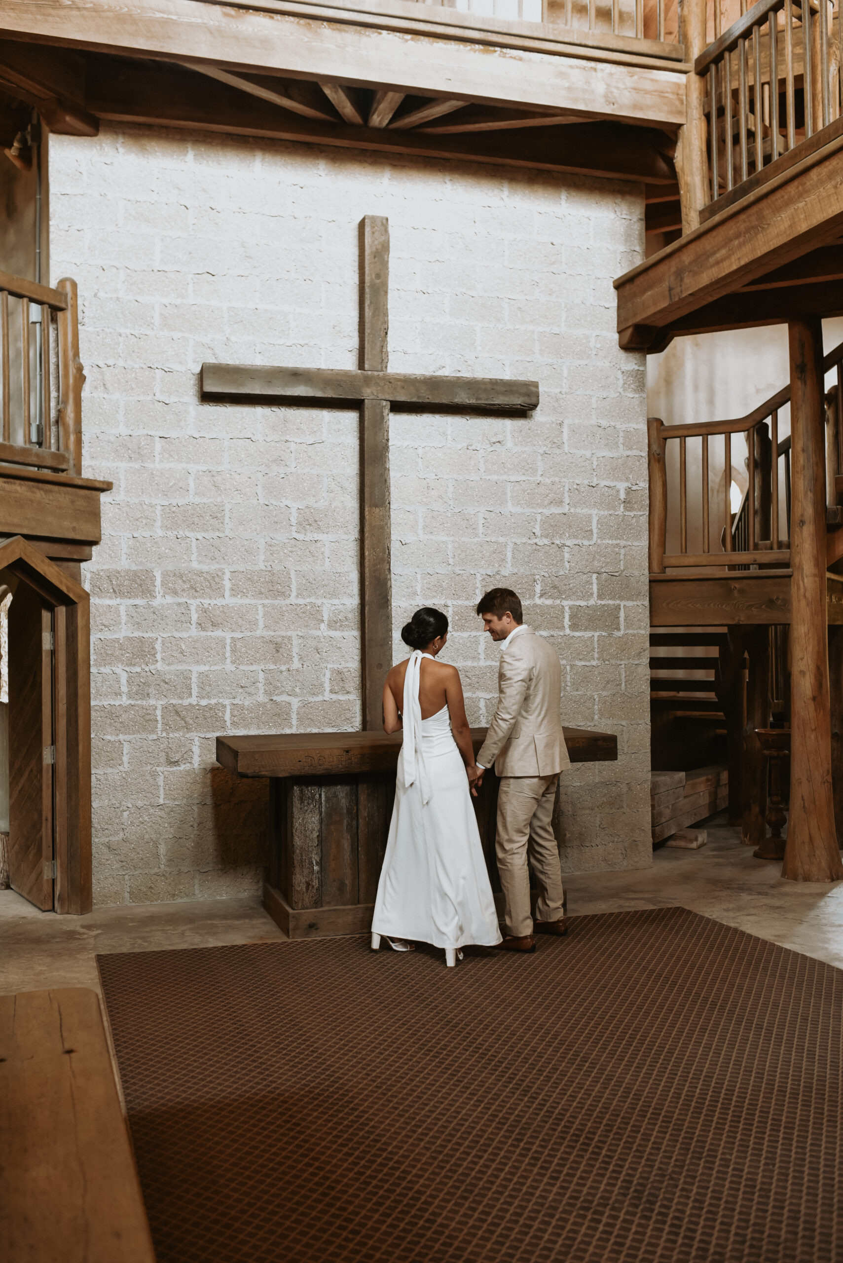 A bride and groom holding hands at a rustic wooden altar beneath a tall timber cross